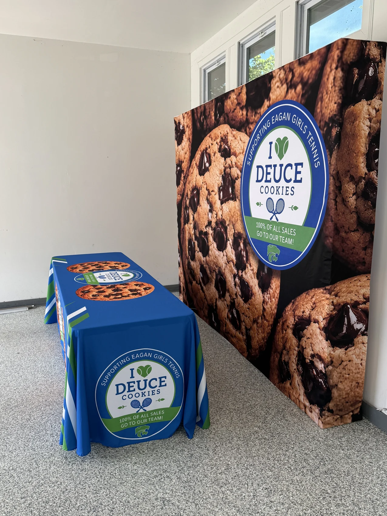 The Deuce Cookies fundraising booth with its cookie backdrop and branded table